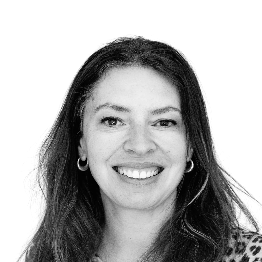 Retrato a preto e branco de Melanie Wadey sorridente, com brincos e camisola com padrão.