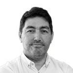 Retrato a preto e branco de Ricardo Luiz, de camisa, sorrindo levemente.