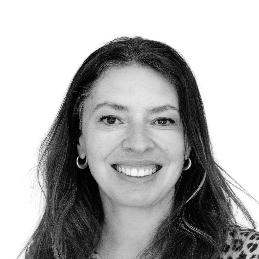 Retrato a preto e branco de Melanie Wadey sorridente, com brincos e camisola com padrão.